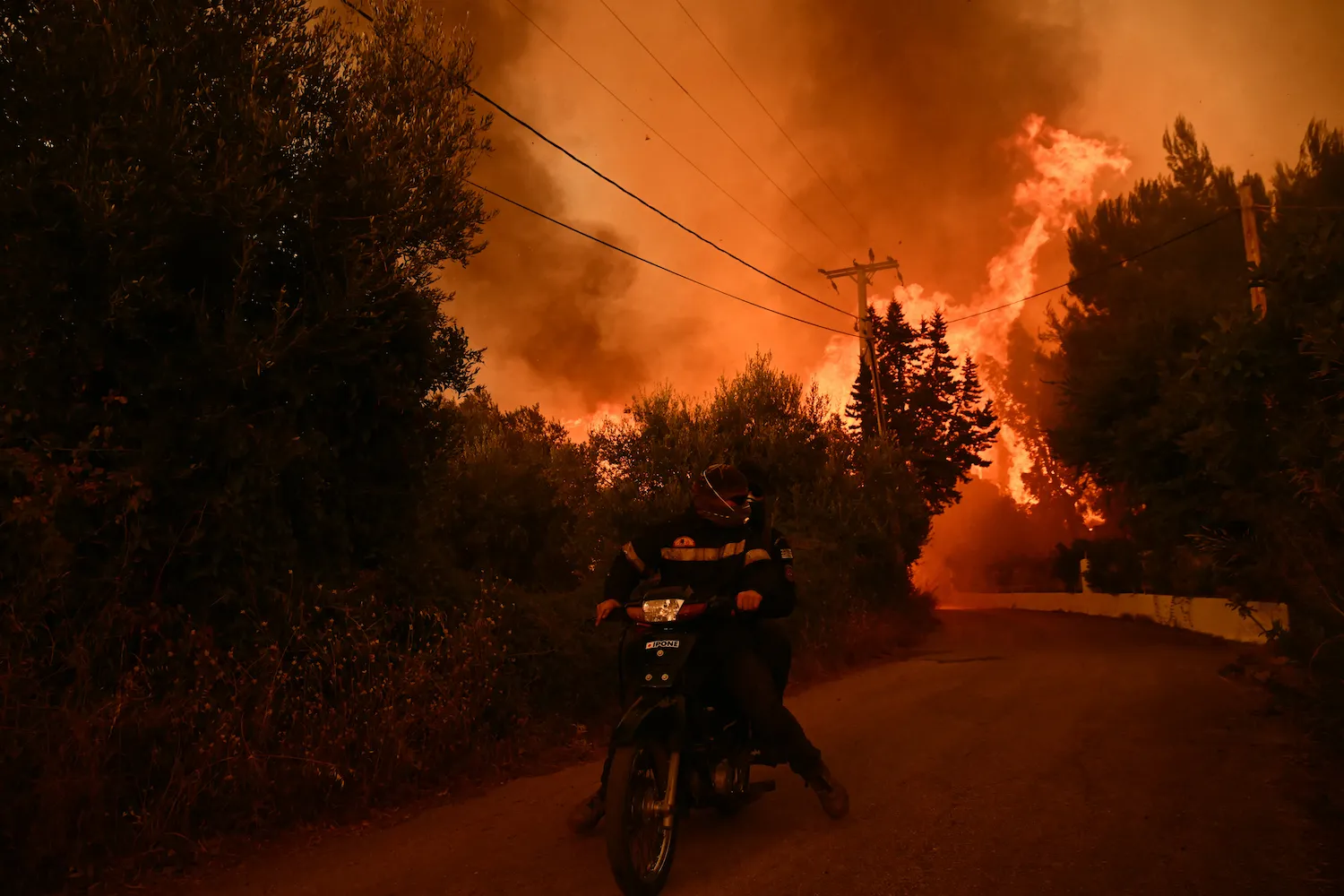 Firefighters leave an area on a scooter as flames approach during a wildfire near the city of Patras, western Greece, on Aug. 13. The country has battled to contain more than 20 wildfires including one menacing its third-largest city, Patras, as a heat wave stoked blazes and forced the evacuation of thousands in southern Europe.